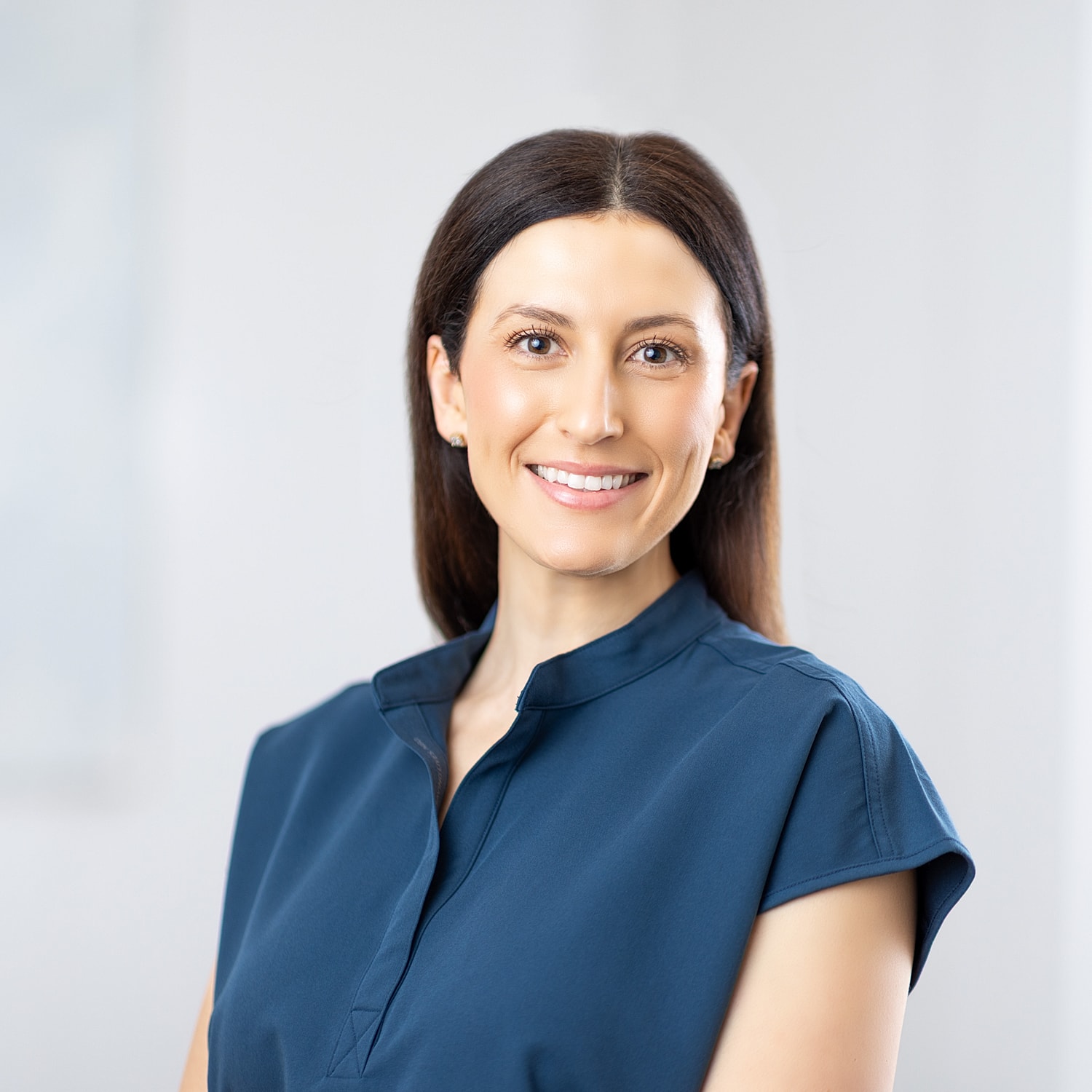 Smiling woman in blue top, neutral background.