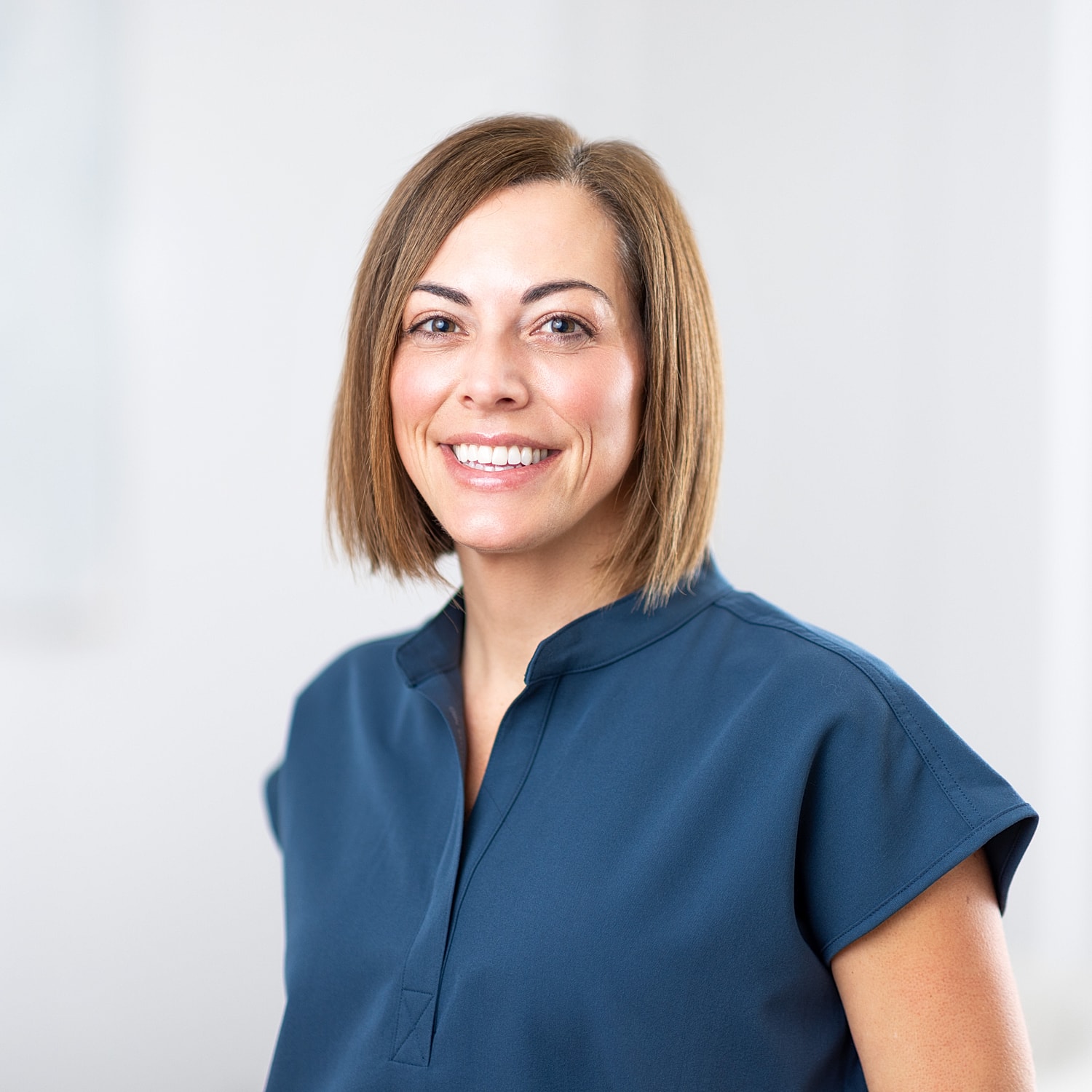 Smiling woman in a blue shirt, neutral background.
