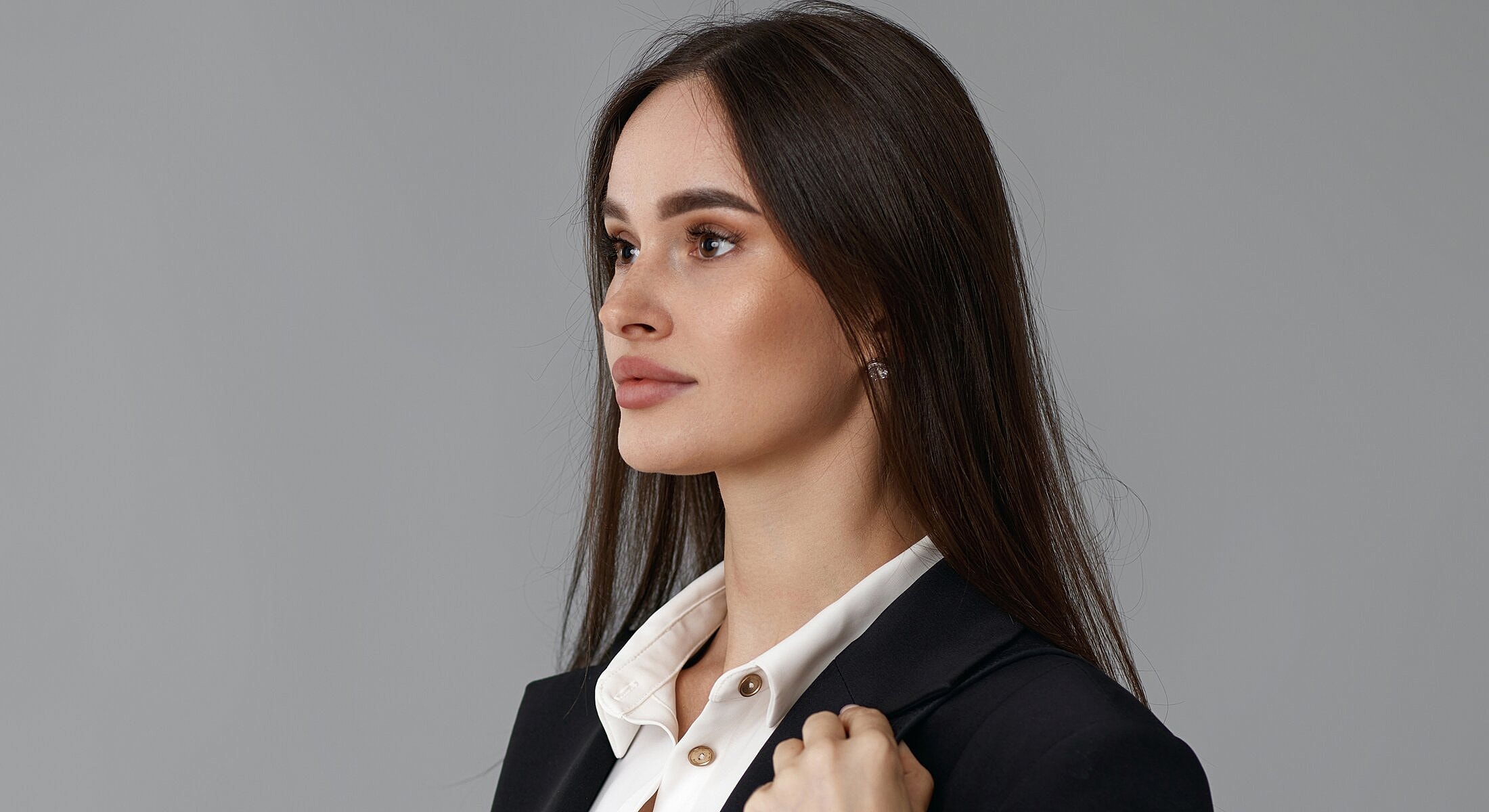Woman in professional attire on gray background.